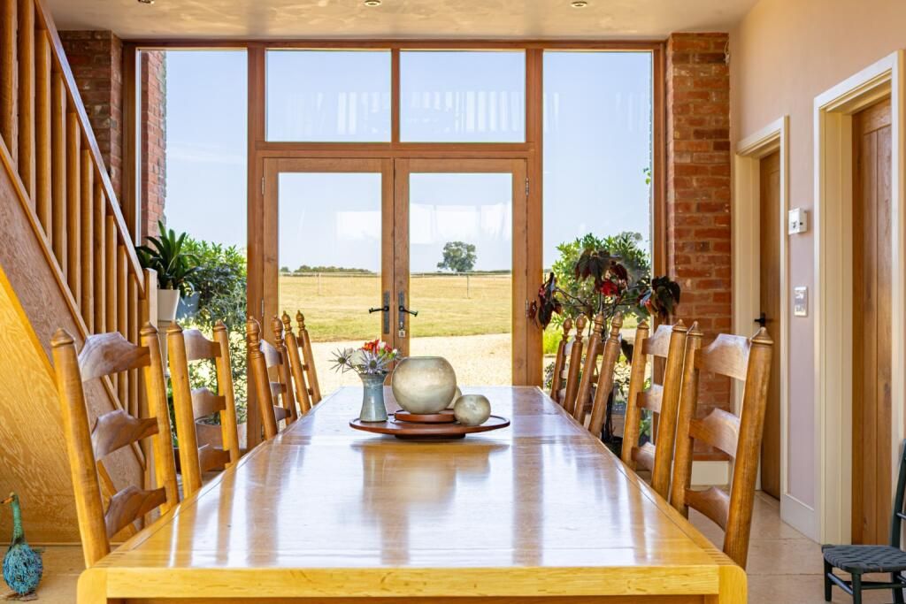 Long oak dining table and ladder-back chairs facing glass doors onto open fields
