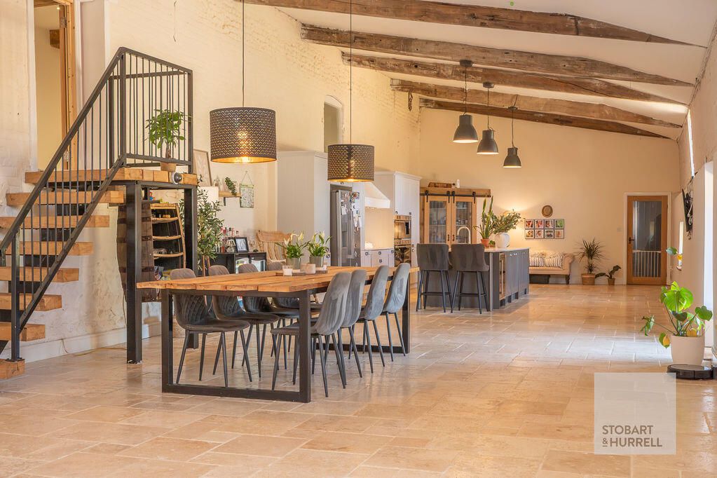 Open-plan barn with a long dining table, kitchen island and exposed roof beams