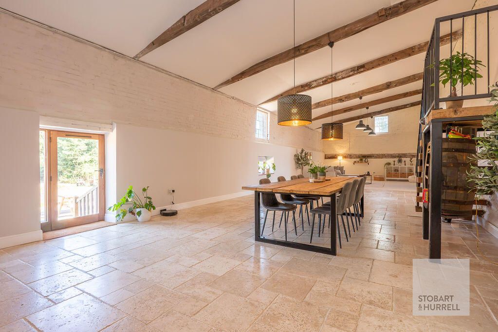 A long beamed room with a wooden dining table and pendant lights