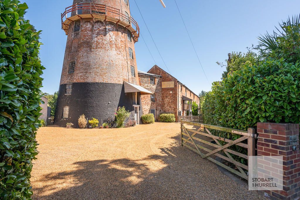 The windmill tower and barn behind a five-bar gate and gravel drive